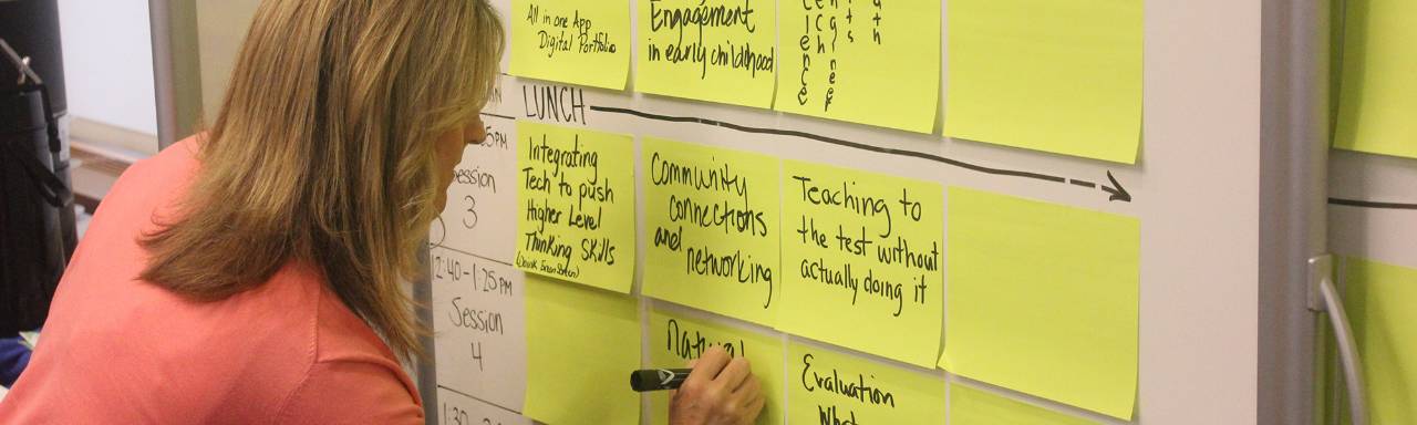 Woman writing notes on a whiteboard filled with sticky notes